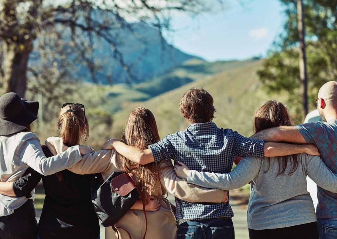 A group of people standing arm in arm, looking out over green mountains on a sunny day